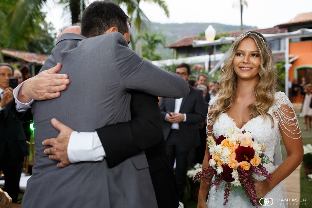 Noivo abraçando pai da noiva e recebendo noiva no altar em casamento judaico ao ar livre no Solar das Palmeiras na ilha da gigoia RJ por Dantas Jr