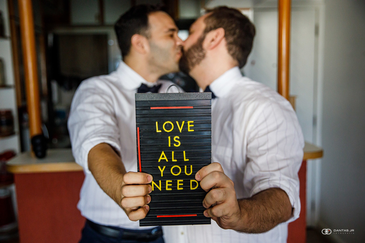 casal gay se beijando e segurando plaquinha escrita All You Need is Love por Dantas Jr.