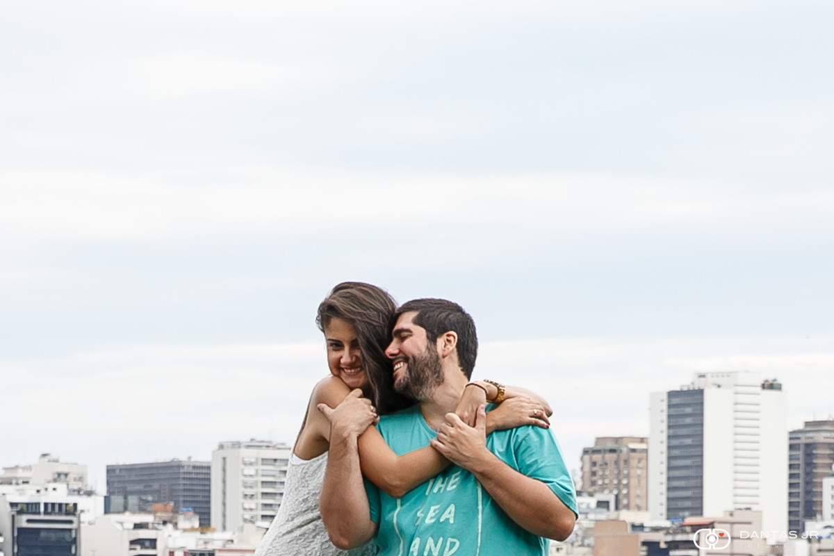 Casal se abraçando e rindo apaixonado em ensaio pre wedding na Lagoa Rodrigo de Freitas com prédios ao fundo por Dantas Jr. Fotografia