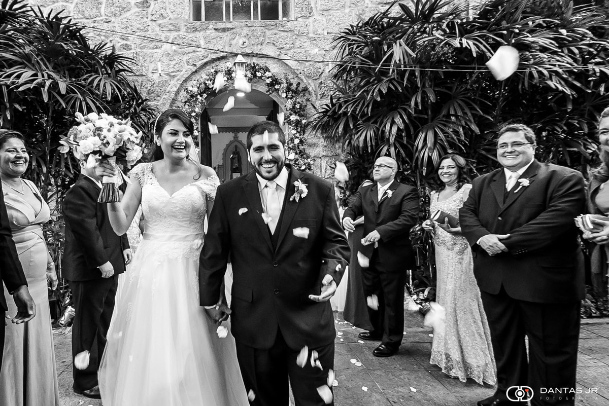 Casal de noivos saindo feliz da cerimônia de casamento na paróquia de Santa Ignez na Gávea sob chuva de arroz e bolas de sabão por Dantas Jr. Fotografia