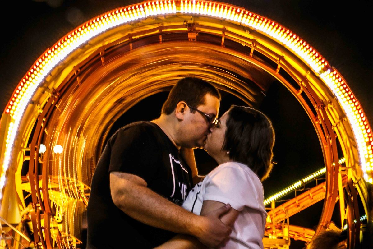 Casal se beijando em ensaio com montanha russa em movimento ao fundo