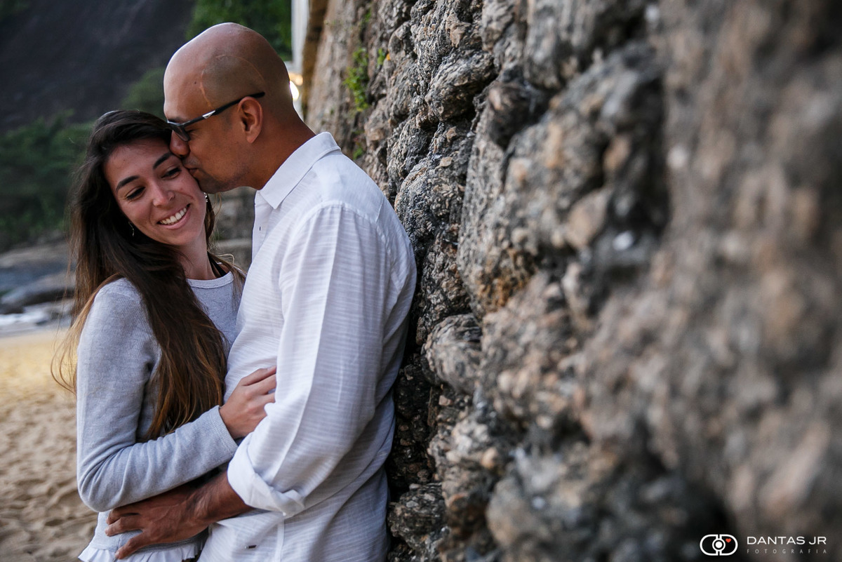 casal de noivos se beijando encostado em muro de pedras
