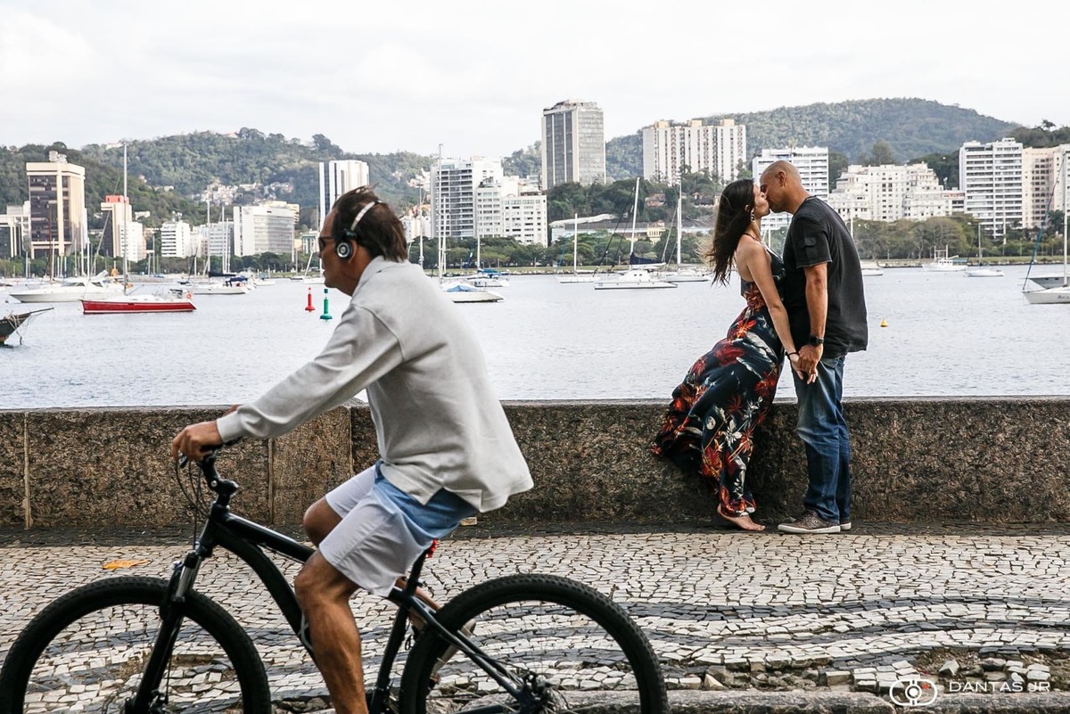 casal de noivos de sao paulo em destination wedding e ensaio prewedding no Rio de Janeiro se beijando na mureta da Urca enquanto homem passa pedalando bicicleta fotografados por Dantas Jr. Fotografia
