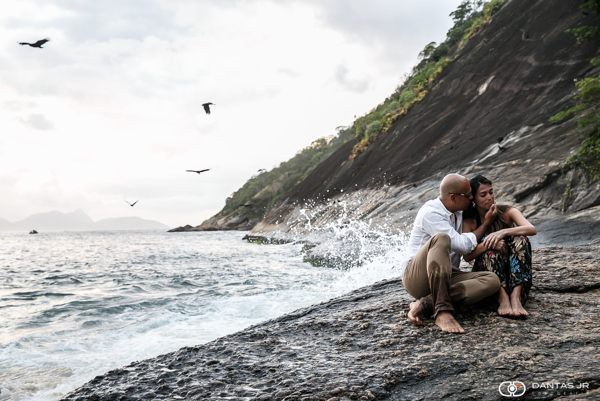casal de noivos na pedra com mar batendo e pássaros voando ao fundo