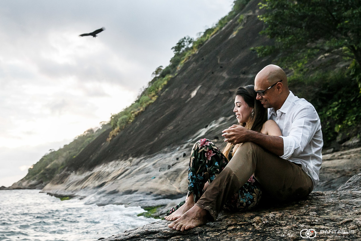 casal namorando nas pedras de praia deserta com pássaros voando