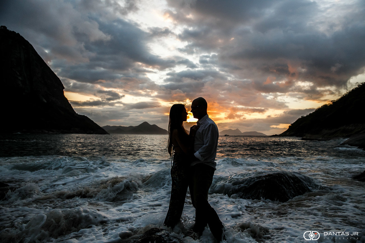 casal se beijando no nascer do sol com água batendo nos pés  e praia deserta
