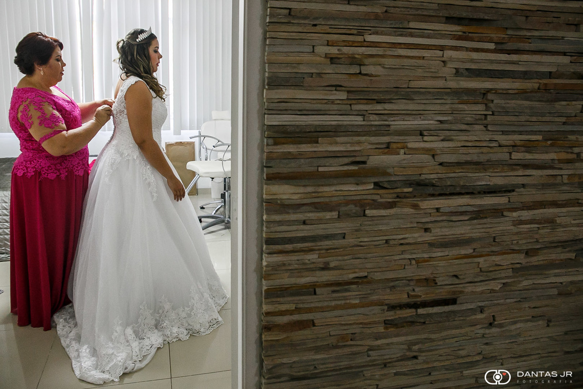 mãe da noiva fechando vestido vista pela porta em making of