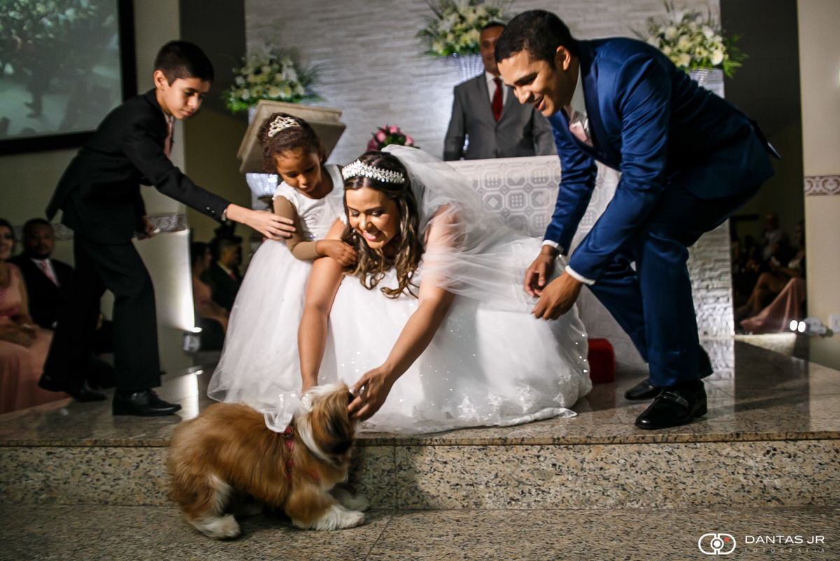 casal de noivos recebendo cachorrinho de estimação com alianças no altar de igreja em cerimônia de casamento