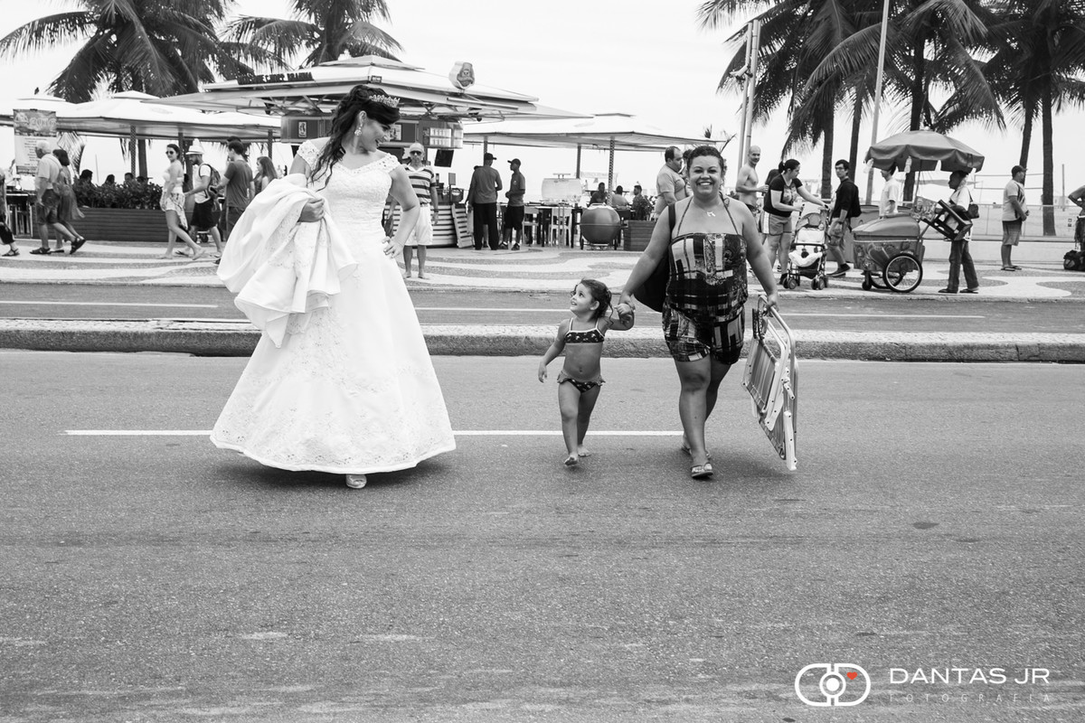 Noiva atravessando a rua no calçadão de Copacabana num dia de sol e praia e sendo observada por uma criança