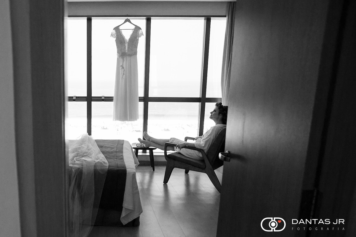 noiva relaxando em quarto de hotel com vista para a praia de Copacabana e vestido pendurado
