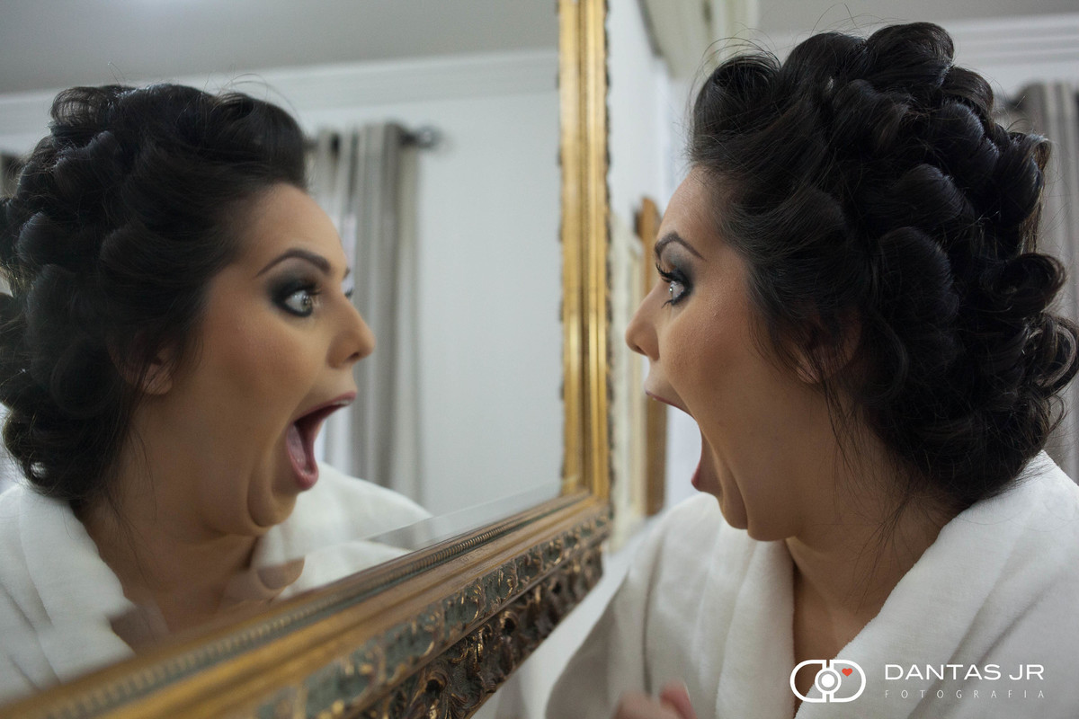 noiva se olhando no espelho com cara de surpresa e espanto feliz com a maquiagem antes do casamento