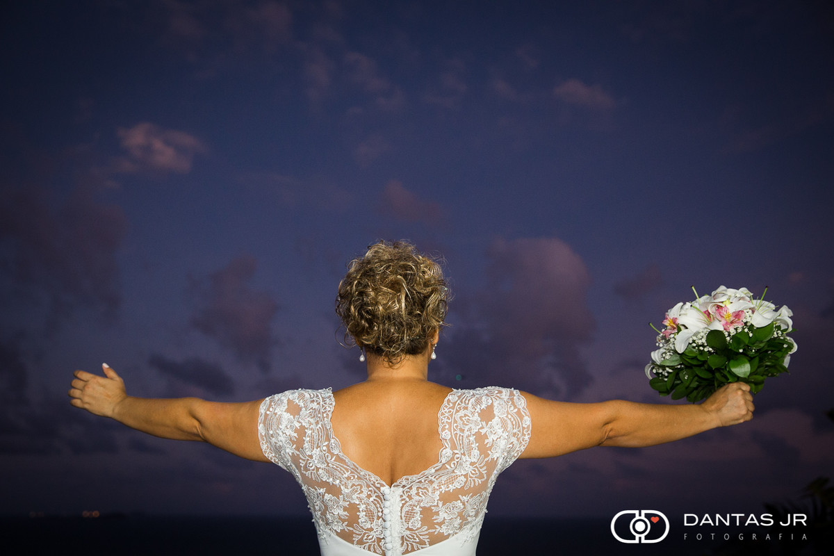 noiva de braços abertos de costas no por do sol