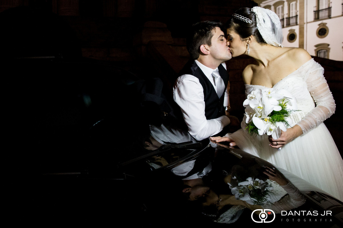 noivos se beijando sobre carro preto com reflexo