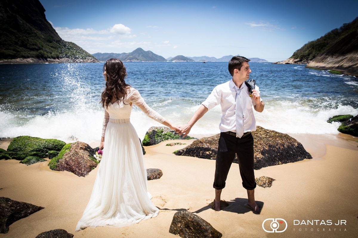 noivos de mão dada olhando cada um pra um lado em trash the dress na praia