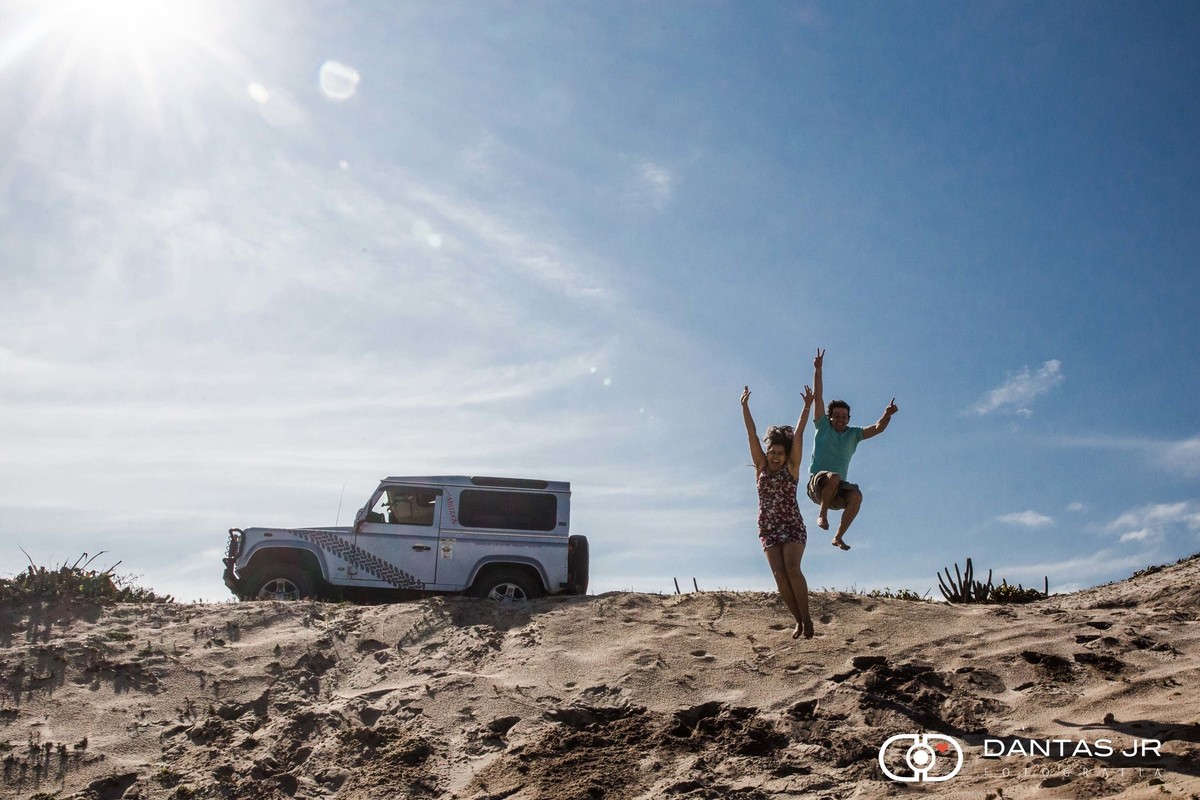casal saltando do alto de dunas em pre wedding nas dunas do buraco da aeronautica com jipe ao fundo clicados por Dantas Jr