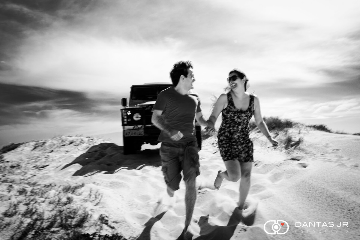 casal correndo nas dunas com jipe ao fundo
