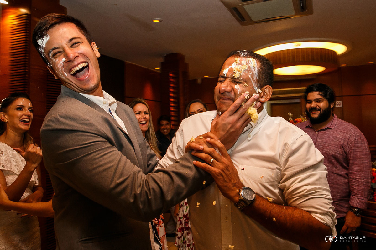 noivo passando fatia de bolo na cara de um padrinho