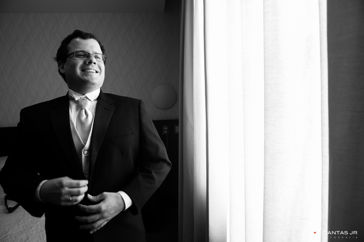 noivo se arrumando no making of perto da janela sorrindo por Dantas Jr.