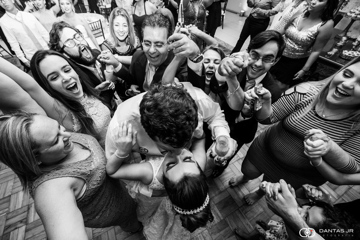 Casal de noivos se beijando com convidados amigos e familiares em volta felizes dançando em festa de casamento na Casa do Minho no Cosme Velho no Rio de Janeiro por Dantas Jr.
