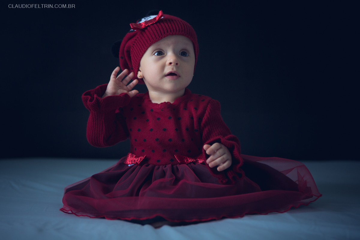 criança posando para ensaio infantil, com vestido vermelho colocando a mão no ouvido como se não estivesse ouvindo