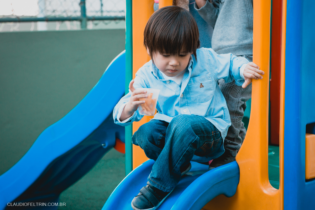 aniversariante escorregando no escorregador com um copo cheio de batatinhas fritas na mão