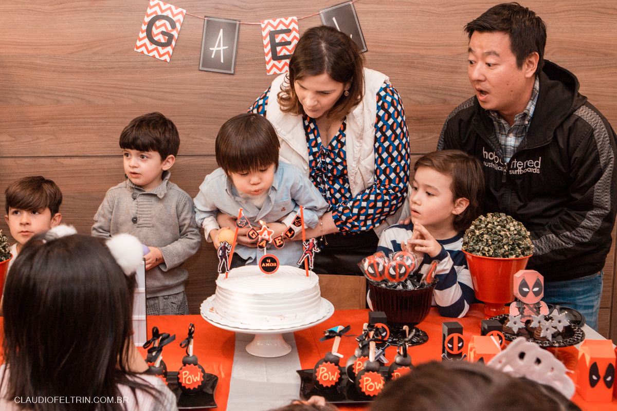 mãe ajuda o aniversariante a apagar a vela de 4 anos e o pai faz uma cara de surpreso 