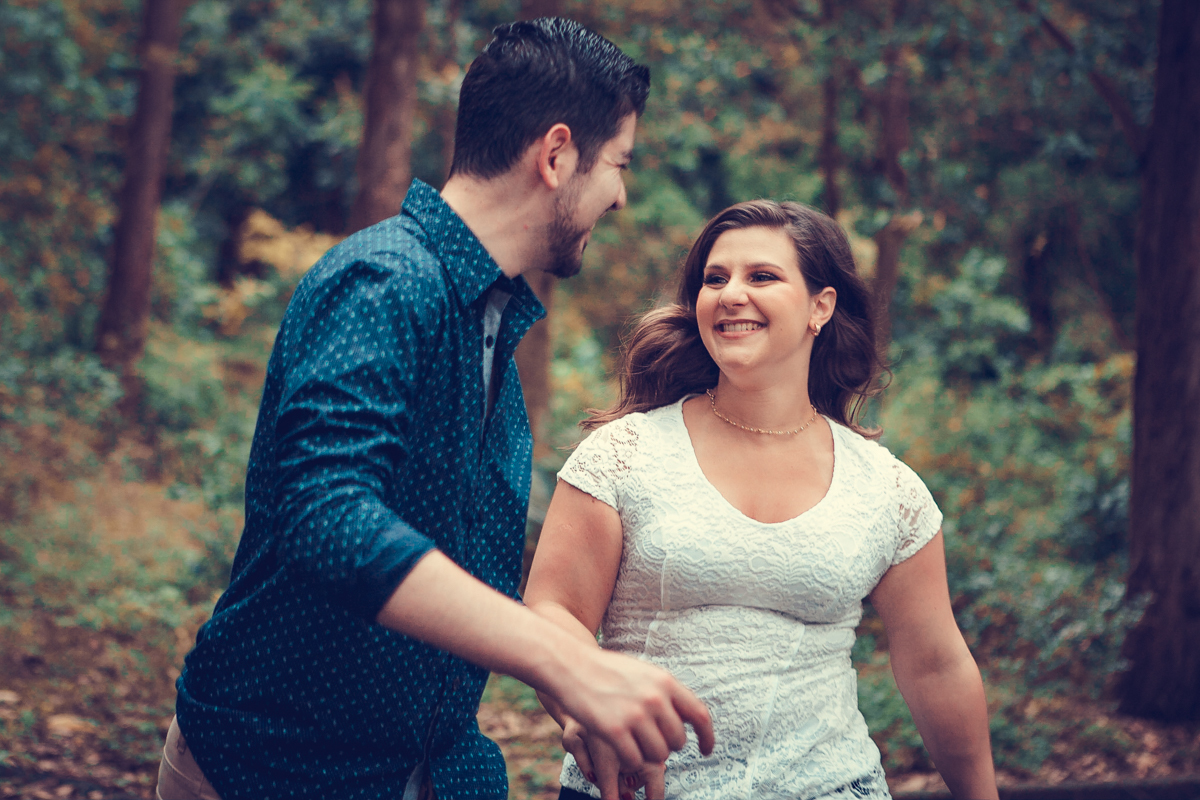 em meio a muitas arvores os noivos correm de mãos dadas em ensaio fotográfico