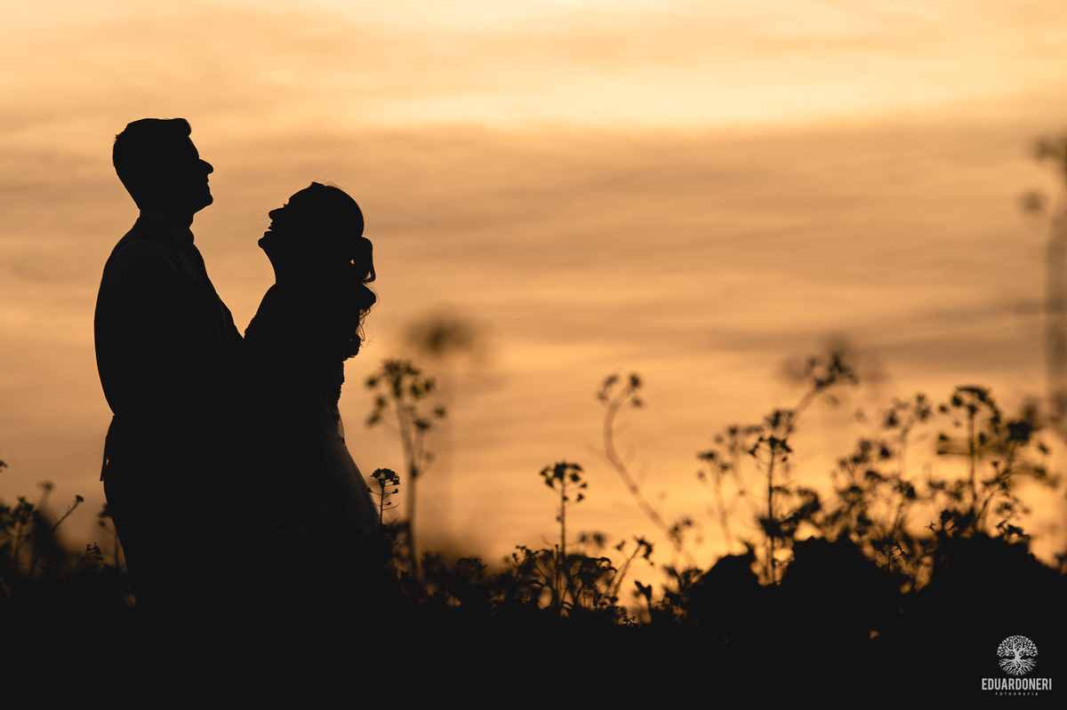 Casal se abraçando sob o céu alaranjado ao final de um Trash the Dress inesquecível