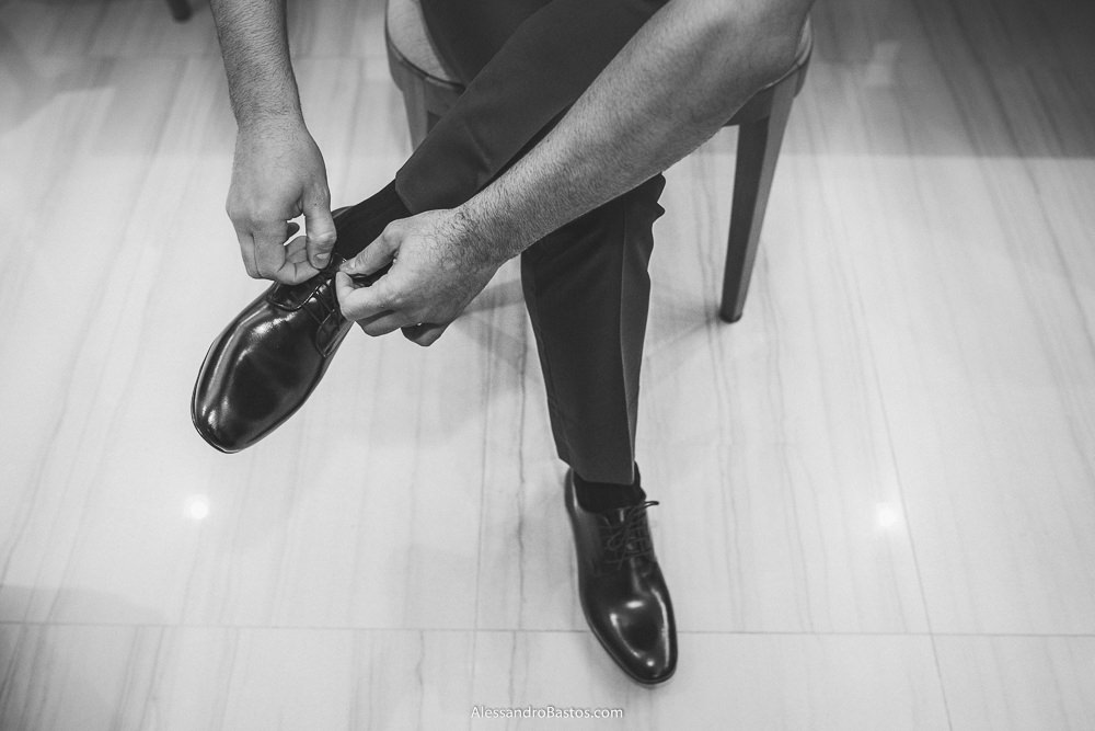 amarrando o sapato está o noivo do casamento em belo horizonte bh foto sentando em uma cadeira em sua casa