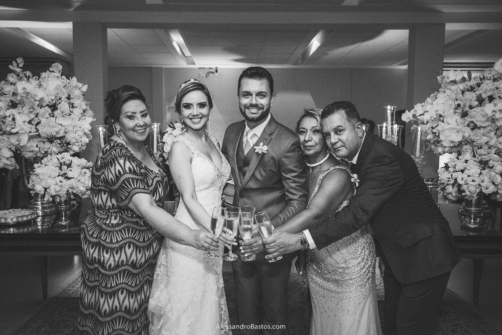 brindando estão os noivos do casamento em belo horizonte bh foto e seus pais na frente do bolo
