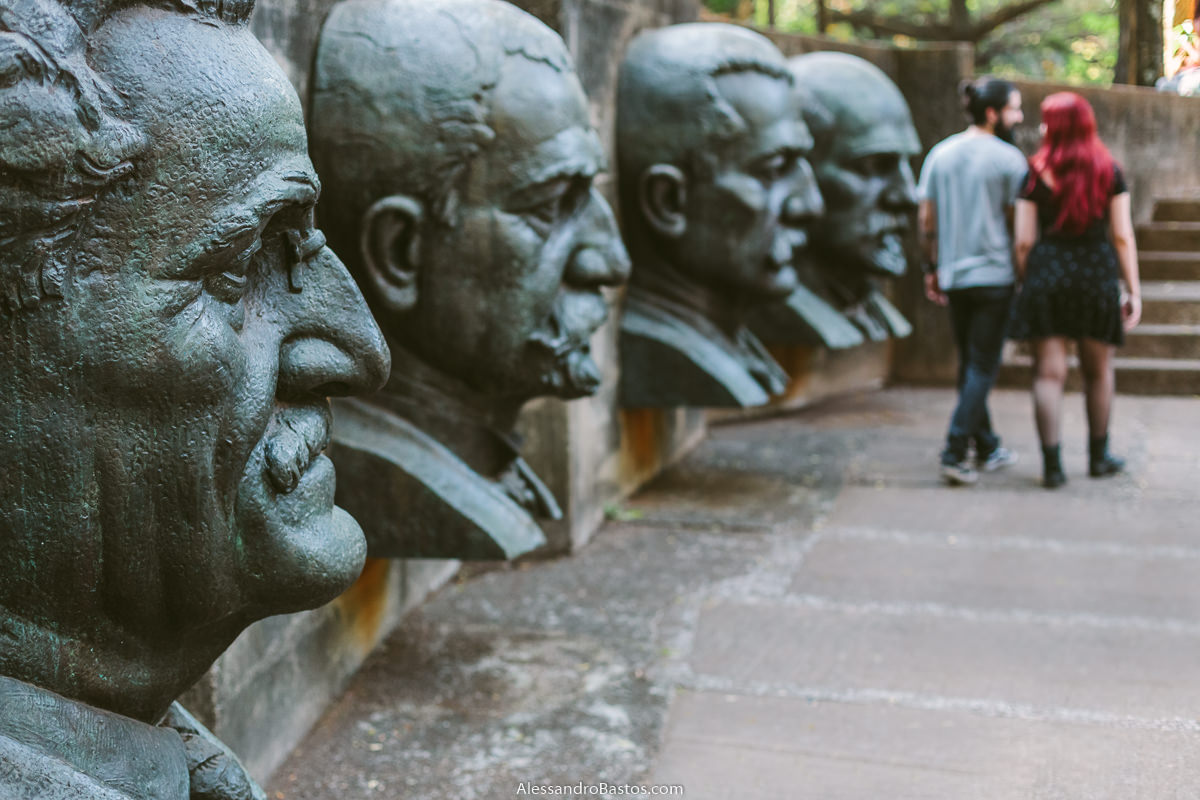 quatro rostos de políticos observam os noivos em sessão de fotografia pré-wedding antes do casamento em bh caminhando na frente deles em um domingo