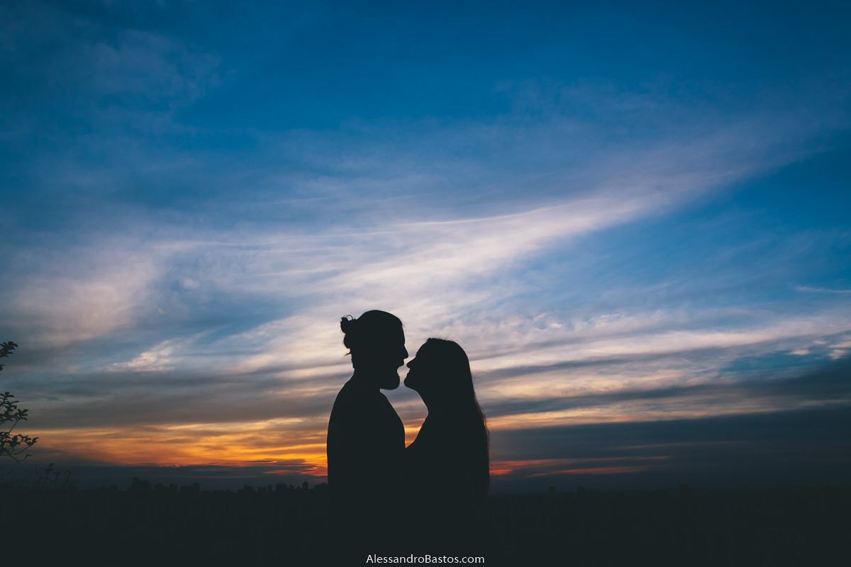 sol se pondo com os noivos em sessão de fotografia pré-wedding antes do casamento em bh contra a luz e um céu azul intenso