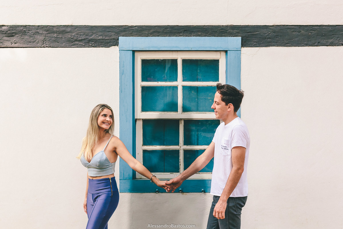 caminhando em frente a uma janela azul na fotografia pre-wedding fotografo casamento bh os noivos seguem