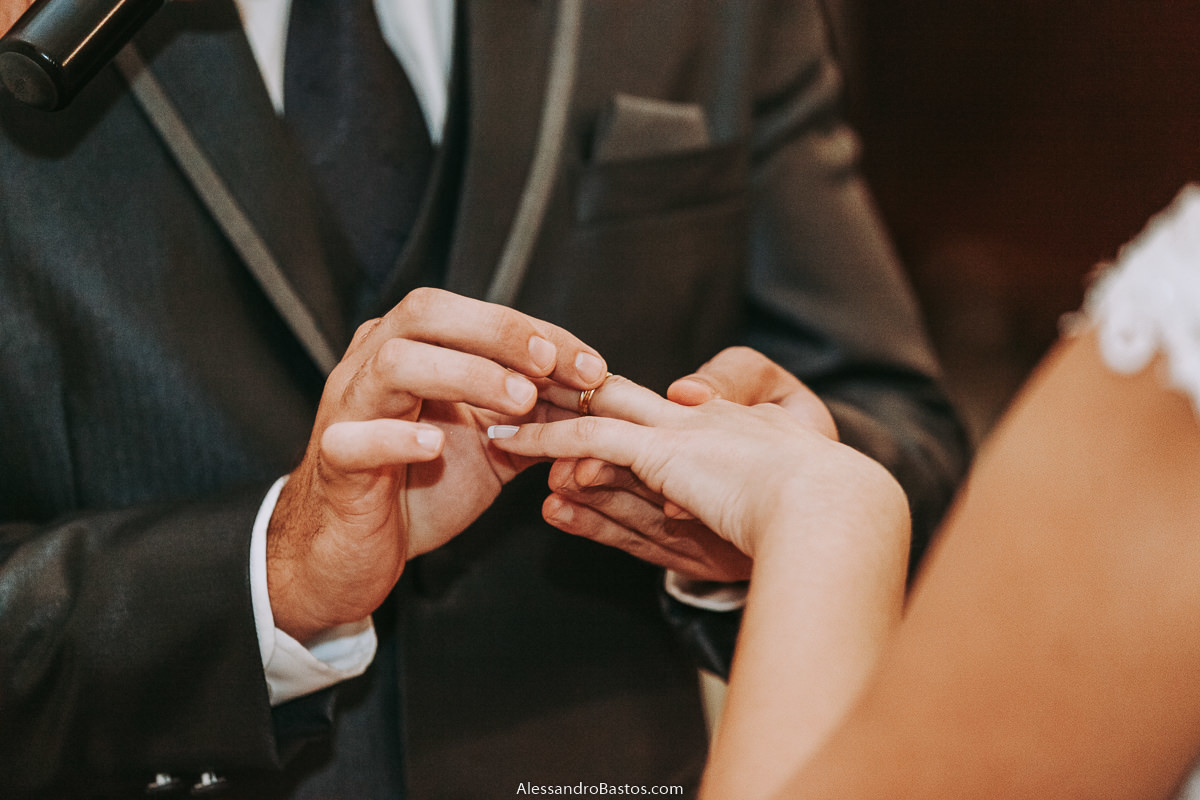 colocando a aliança no dedo na noiva fotografo casamento bh pre-wedding pre-casamento pos-casamento fotografia belo horizonte santo cura d'ars aparece no fundo a gravata