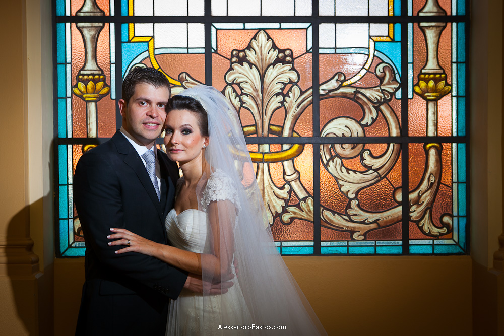 vitral serve de cenário nas fotos do casamento em bh no buffet catharina dos noivos na fotografia em belo horizonte para o fotografo bh no museu de artes e ofícios e os noivos olhando para a câmera