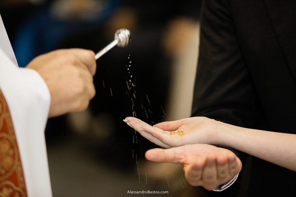 água benta nas alianças nas fotos do casamento em bh na igreja nossa senhora rainha em belo horizonte e a festa para fotografia dos noivos no jardim canada eventos para o fotografo e os noivos seguram elas com as mãos sobrepostas