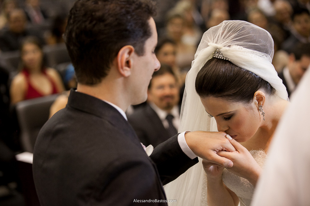 beijando a mão do noivo está a noiva nas fotos do casamento em bh na igreja nossa senhora rainha em belo horizonte e a festa para fotografia dos noivos no jardim canada eventos para o fotografo e ao fundo vejo o pai dela sorrindo de emoção