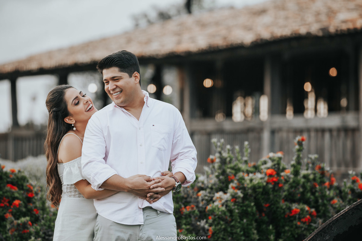 sorrindo os noivos estão no jardim da fazenda solar do engenho para sessão de fotos do pré-wedding com casamento marcado para bh com luzes no fundo do ambiente