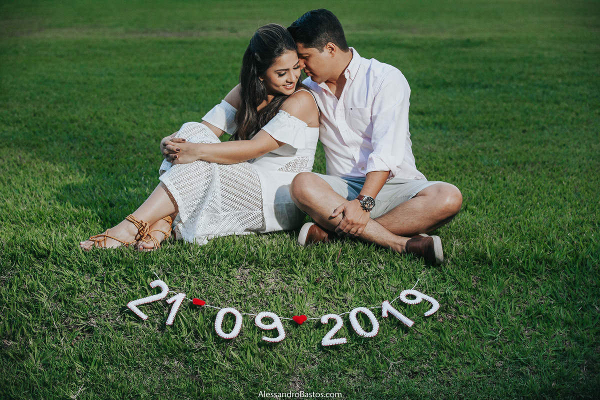 fez a noiva uma plaquinha com a data do casamento bh para usar nas fotos pré-wedding na fazenda solar do engenho com os noivos sentados na grama