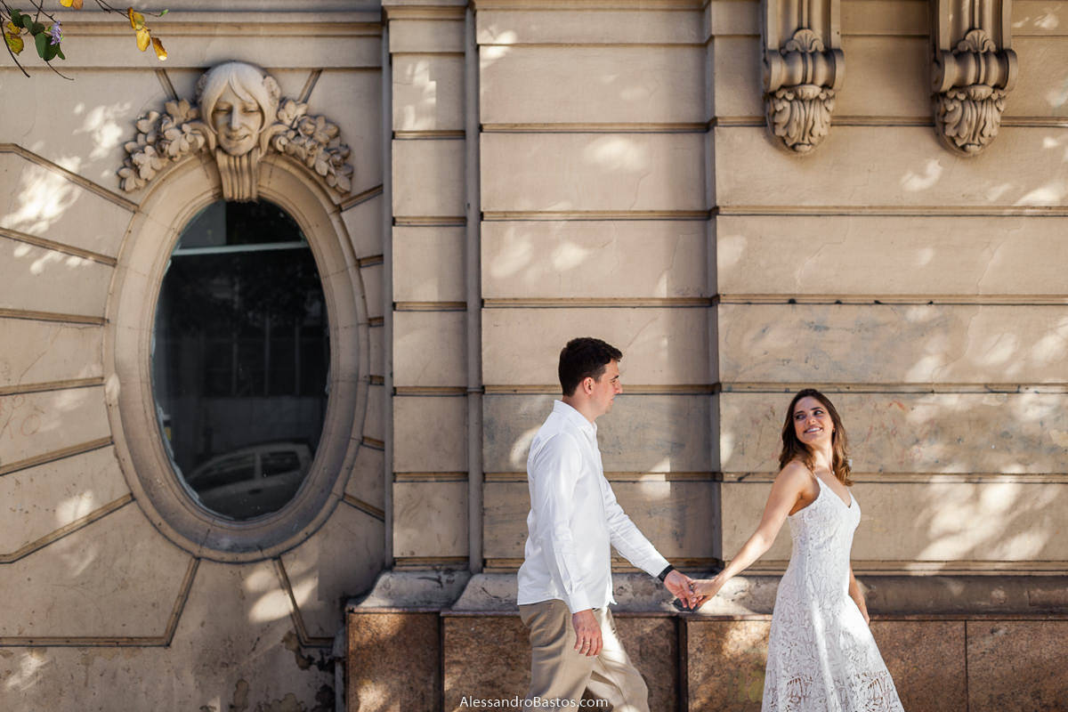 janela com rosto de personagem antigo nas fotos de noivos para casamento em bh fotografo e eles caminhando de mãos dadas na calçada