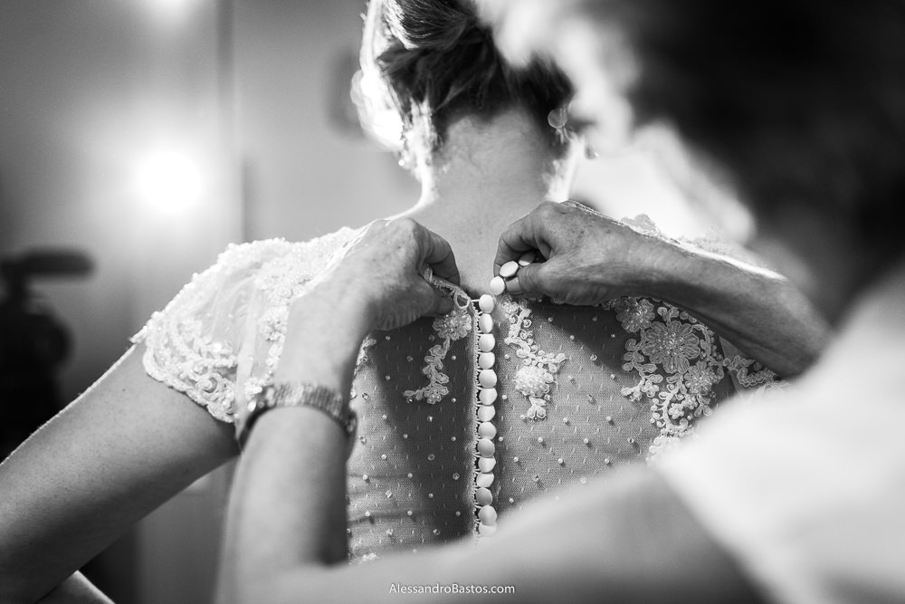 uma assistente do salão do Lazaro Lambertucci em bh ajuda a noiva a colocar o seu vestido fechando os botões nas costas