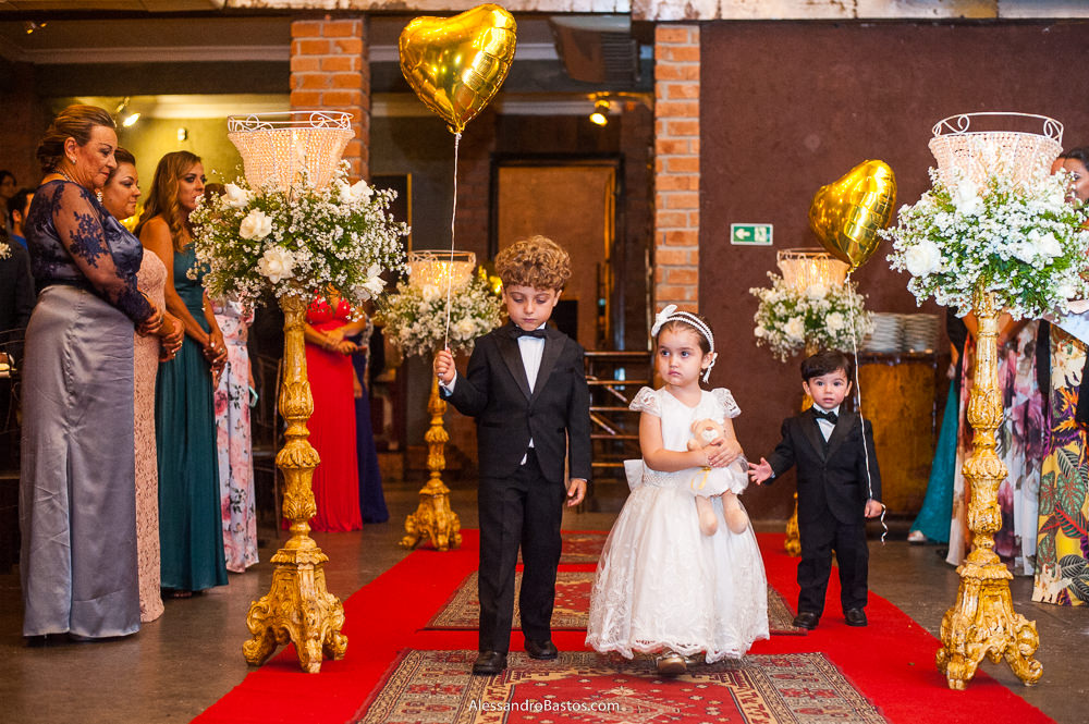 casal de daminha e pajem entra na cerimônia do casamento da Camila no caravaggio ela segurando um ursinho e ele um balão dourado