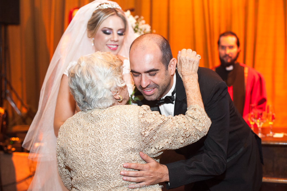 avó nair dá um abraço no noivo gustavo durante a cerimônia do casamento bh no caravaggio e a noiva sorri de felicidade