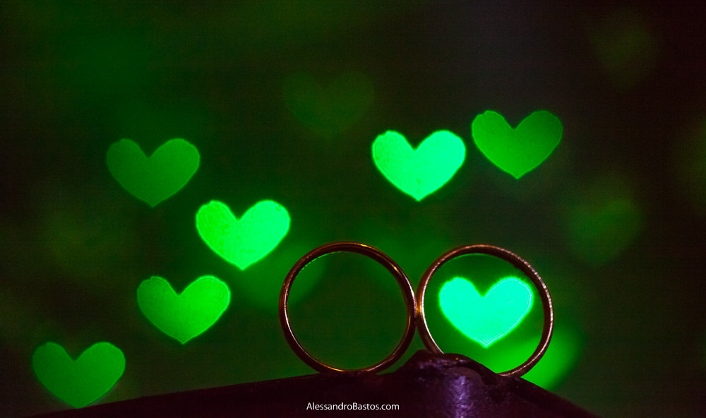 as alianças dos noivos no casamento em bh no caravaggio recebem corações verdes no fundo da foto causado pelas bolas de vidro da boate