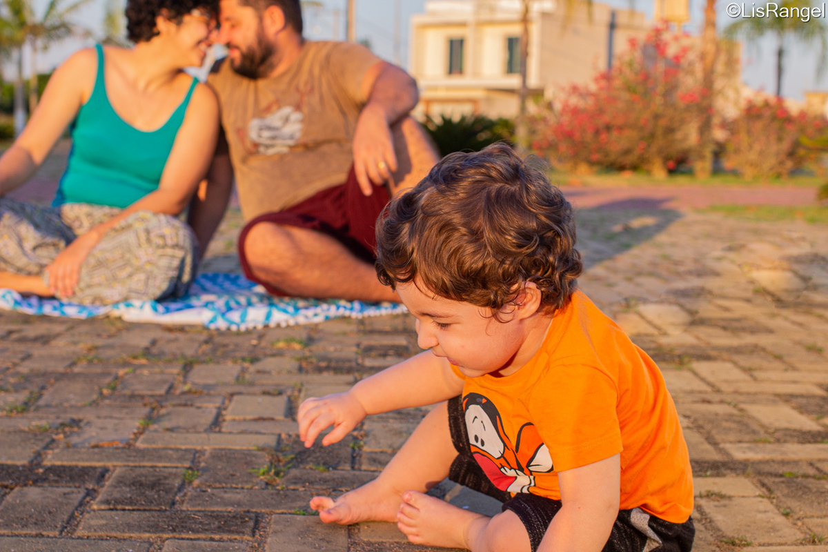 Mãe e pai lado a lado se olhando e o filho brincando na frente deles.