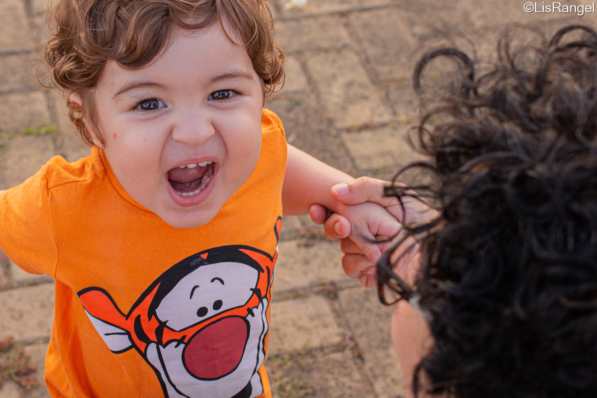 Criança gritando e sorrindo e a mãe segurando ele pelo braço.