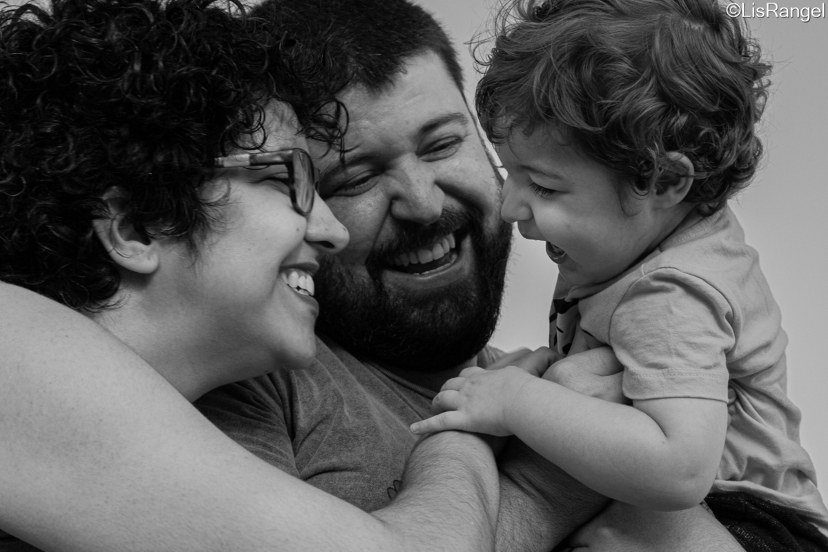 Pai segurando filho que olha para a mãe que está ao lado do pai.