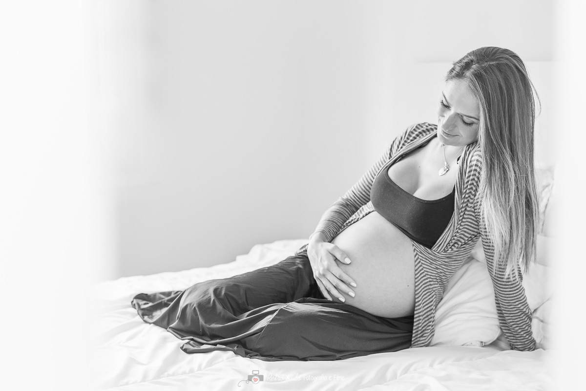 fotografia clean e charmosa segurando a barriga e deitada na cama
