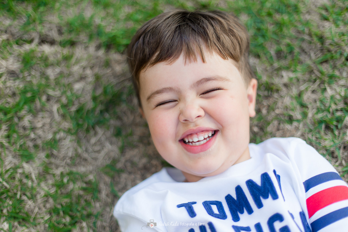 irmã mais velho deitado na grama dando gargalhada de felicidade na festa no condomínio em Tamboré SP
