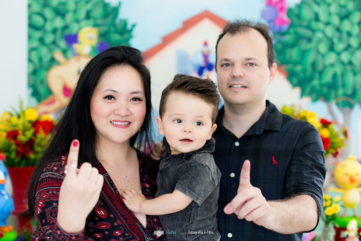 Retrato dos pais com o Guilherme em frente sua mesa de aniversário